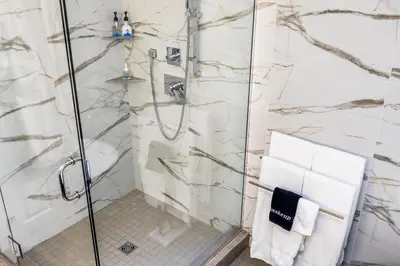 a bathroom with a shower with white marble walls at SKKY Hotel in Whitehorse
