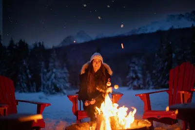 a woman sitting around a fire in the snow at Baker Creek By Basecamp in Lake Louise
