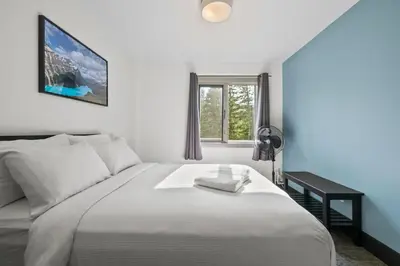a bedroom with a white bed with a desk and a window at HI Lake Louise Alpine Centre - Hostel in Lake Louise