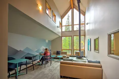 a woman sitting at a table in a room with windows at HI Lake Louise Alpine Centre - Hostel in Lake Louise
