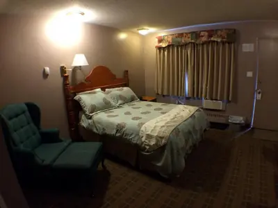 a bedroom with a bed and a chair and a lamp at King's Motel & Restaurant in St. Paul