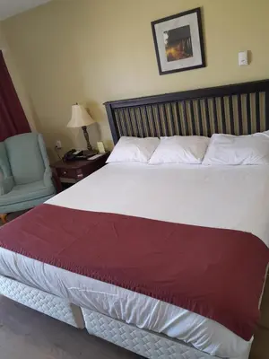a bedroom with a large bed with a chair and a table at Travellers Motel in Cranbrook