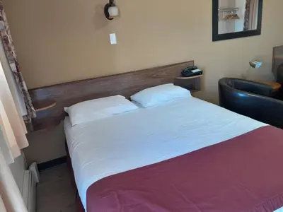 a bedroom with a large bed and a chair at Travellers Motel in Cranbrook