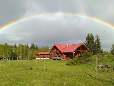 a rainbow in the sky over a log cabin at Cariboo Log Guest House in Lac La Hache