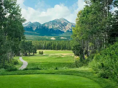a green golf course with mountains in the background at Fitzhugh House Guest Accomodation in Jasper