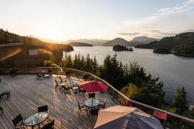a deck with tables and chairs with a view of a lake at West Coast Wilderness Lodge in Egmont