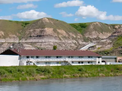 a building next to a river with mountains in the background at Travelodge by Wyndham Drumheller AB in Drumheller