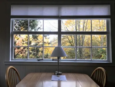 a table with a lamp in front of a large window at Driftwood Village Cottages in Sturdies Bay
