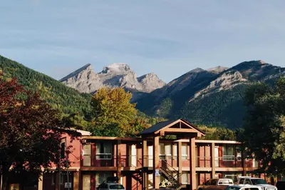 a hotel with mountains in the background with cars parked in front at Canadas Best Value Inn and Suites Fernie in Fernie