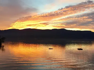 a sunset on a lake with mountains in the background at The Tuwanek Bed and Breakfast in Sechelt