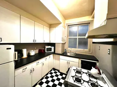 a kitchen with white cabinets and a black and white checkered floor at Arundel Mansions Hotel in New Westminster