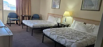 a hotel room with two beds and chairs and a window at Slumber Lodge Williams Lake in Williams Lake