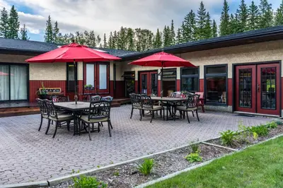 a patio with tables and chairs and red umbrellas at Rustlers Lodge in Sundre