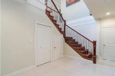 a white hallway with a wooden staircase in a house at Imperial House in Burnaby