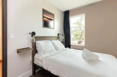 a bedroom with a bed with white sheets and a window at HI Kelowna Hostel in Kelowna