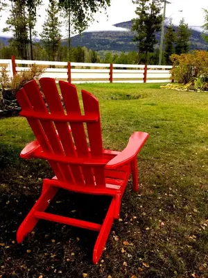 a red chair sitting in the grass near a fence at Rose Cottage Bed & Breakfast in Valemount
