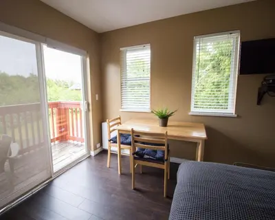 a bedroom with a desk and a bed and a balcony at Reef Point Cottages in Ucluelet
