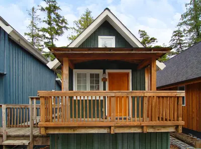 a green house with a porch and a deck at Reef Point Cottages in Ucluelet