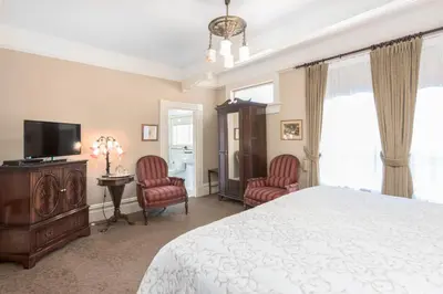 a bedroom with a bed and two chairs and a television at O Canada House Bed & Breakfast in Vancouver