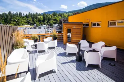 a deck with white chairs and tables and a yellow building at Adventure Hotel in Nelson