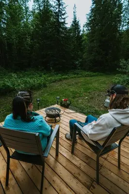 two women sitting on chairs on a deck with a fire at Across the Creek Cabins in Clearwater
