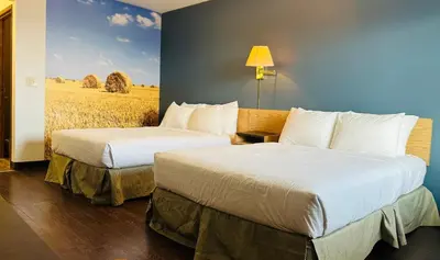 two beds in a hotel room with a mural of a field at Rimbey Motor Inn in Rimbey