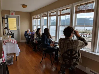 a group of people sitting at tables in a room with windows at Nimpkish Hotel in Alert Bay