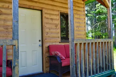 a porch of a log cabin with a red couch at Schott's Lake Conference & Resort in Sundre