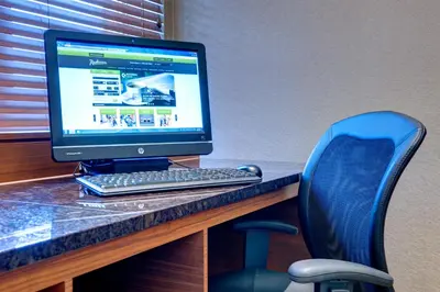 a computer monitor sitting on a desk with a blue chair at Radisson Hotel & Suites Fort McMurray in Fort McMurray