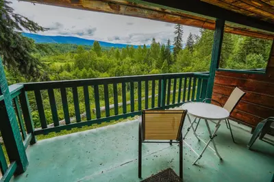 a table and chair on a porch with a view at Helmcken Falls Lodge Cabin Rooms and RV Park in Clearwater