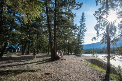 three people sitting on a tree stump near a lake at Pine Bungalows in Jasper