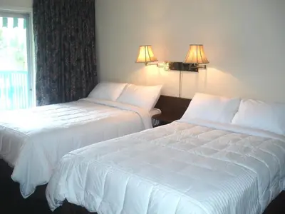 two beds in a hotel room with white sheets at Motel Tyrol in Radium Hot Springs