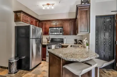 a kitchen with wooden cabinets and a stainless steel refrigerator at The Mountaineer by InstantSuites Pool & HotTub in Canmore