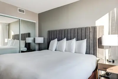 a large white bed in a hotel room with a mirror at Carmana Hotel & Suites in Vancouver