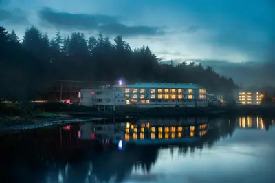 a building with lights on next to a river at night at Glen Lyon Inn in Port Hardy