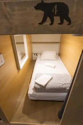 a small bed in a room with a bear on the wall at The Raging Elk Adventure Lodging in Fernie