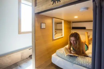 a girl laying on a bunk bed reading a book at The Raging Elk Adventure Lodging in Fernie