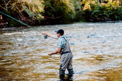 a man standing in a river holding a fishing rod at Cowichan River Lodge in Lake Cowichan