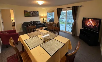 a living room with a table and a tv at Bayshore Waterfront Inn in Ucluelet
