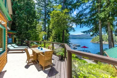 a deck with a table and chairs and a view of a lake at Tranquility Bay Waterfront Inn in Sechelt