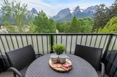 a table with two chairs on a balcony with mountains at Heavenly Mountain Condo managed by Little Sister Getaways in Canmore