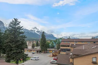a town with cars parked in a parking lot with mountains at Heavenly Mountain Condo managed by Little Sister Getaways in Canmore