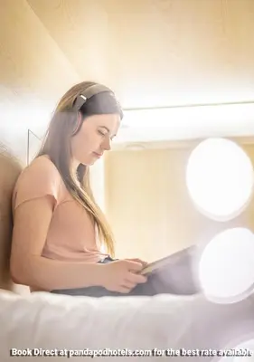 a woman sitting on a bed reading a book at Panda Pod Hotel in Richmond