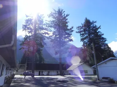 a building with trees in front of a mountain at Skagit Motel in Hope