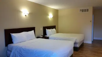 two beds in a hotel room with white sheets at Comox Valley Inn & Suites in Courtenay