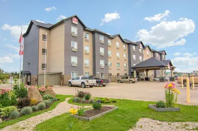 a large building with cars parked in a parking lot at Devonian Hotel and Suites in Fox Creek