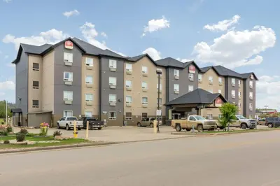 a large apartment building with cars parked in a parking lot at Devonian Hotel and Suites in Fox Creek