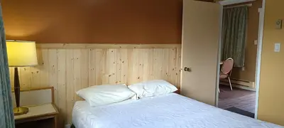 a bedroom with a bed with white sheets and a lamp at Gold Pan Motel in Quesnel