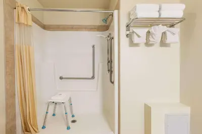 a bathroom with a shower with a stool and towels at Days Inn by Wyndham Chetwynd in Chetwynd