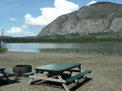 a picnic table on a beach next to a lake at Parkside Inn in Haines Junction